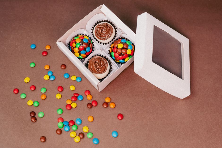 Vibrant candy cupcakes in a white box against a brown background, perfect for food photography.