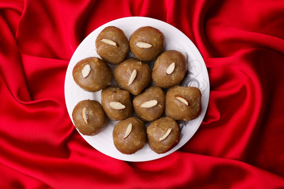 Top view of traditional Indian sweets garnished with almonds on a white plate over red fabric.