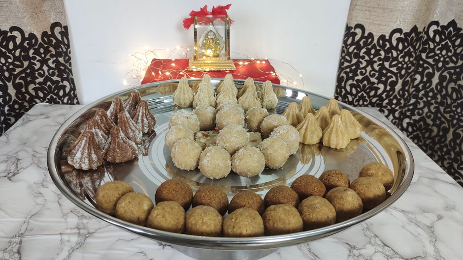 Assorted Indian modak sweets and ladoos on a silver platter, symbolizing festive celebrations.
